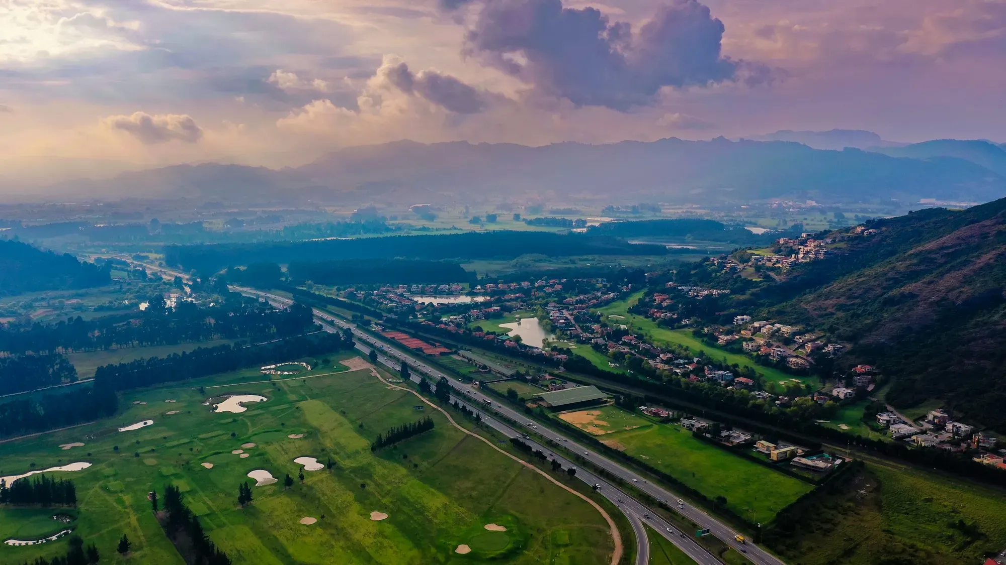 Vista aérea de una autopista que atraviesa un valle verde rodeado de montañas al atardecer