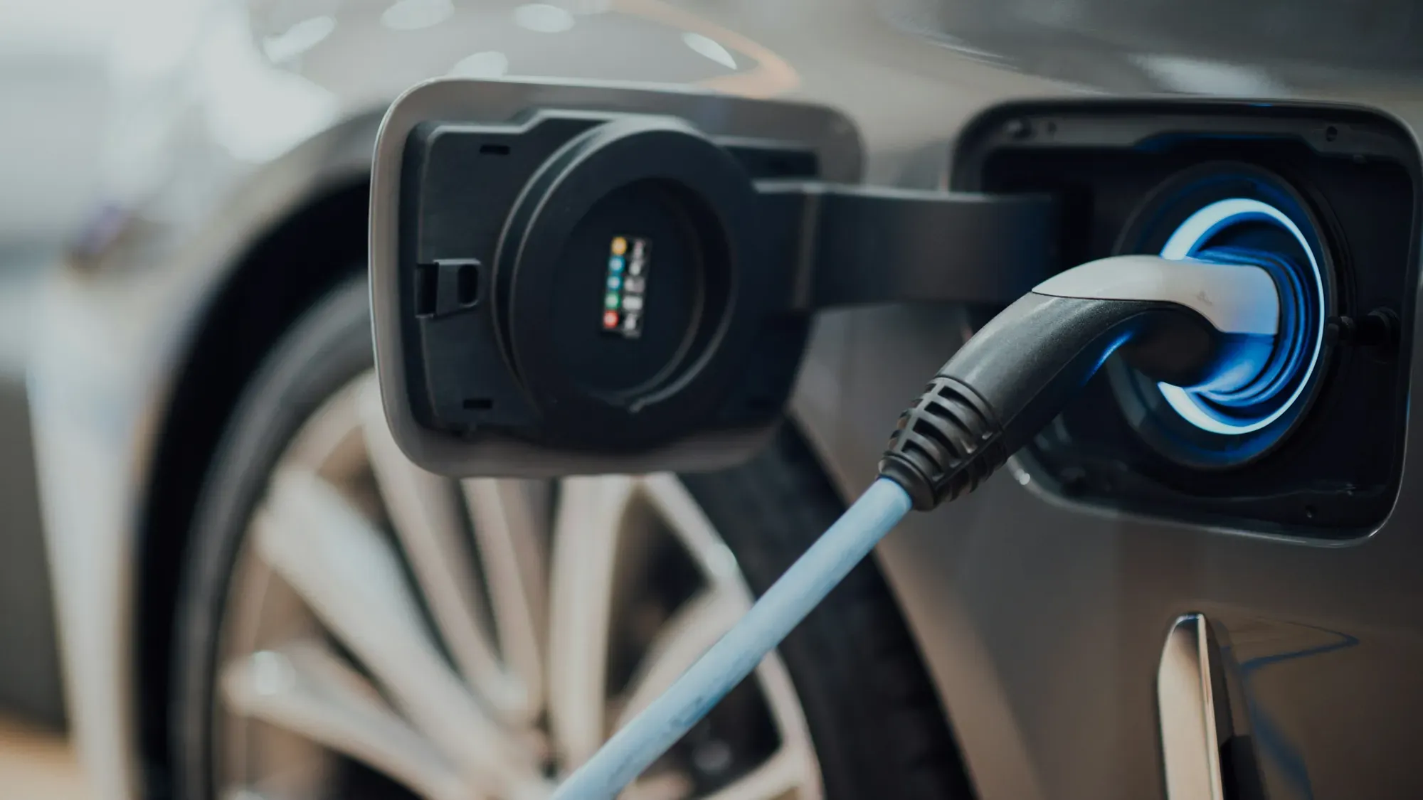Cable de carga conectado al puerto de un carro eléctrico plateado