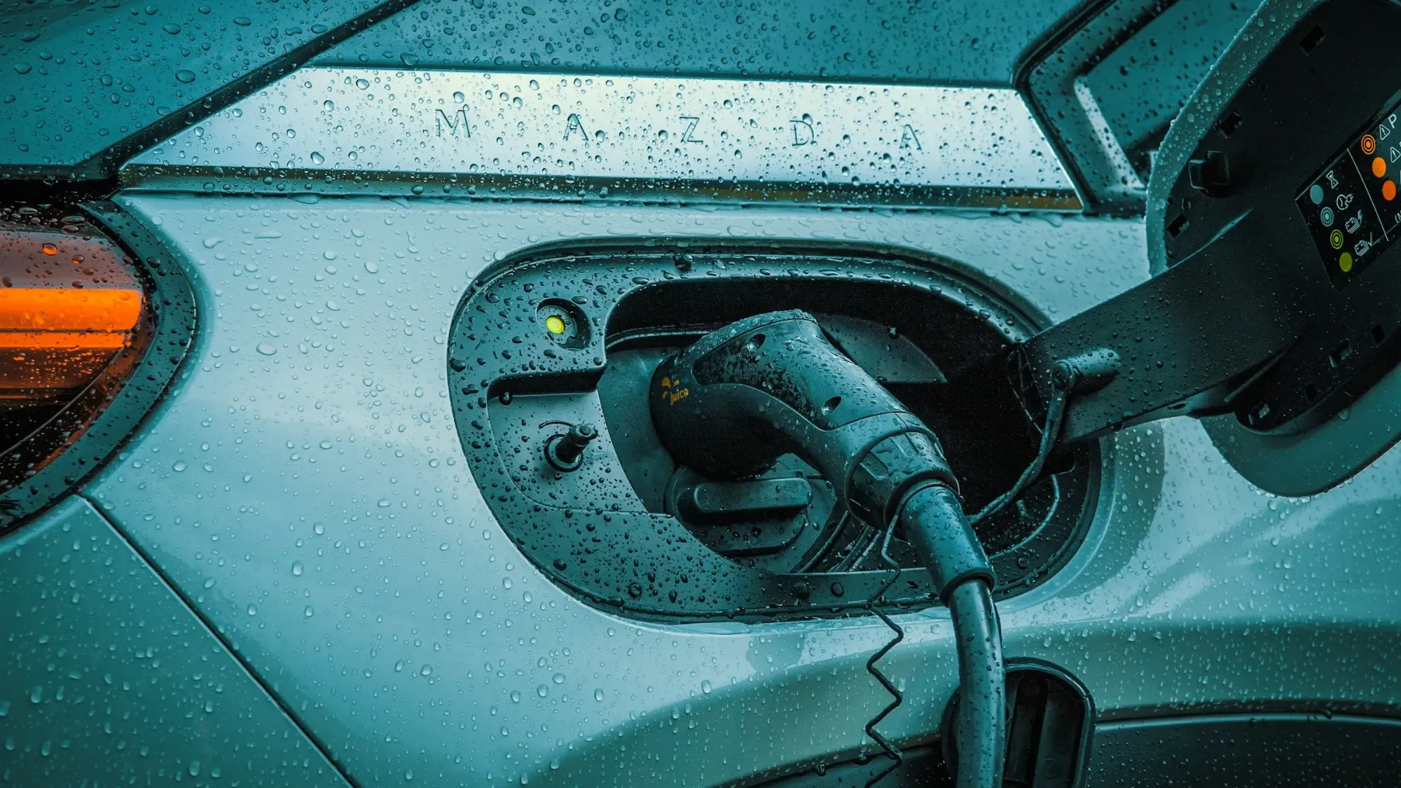 Conector de carga enchufado en el puerto de un carro eléctrico, con gotas de lluvia en la carrocería