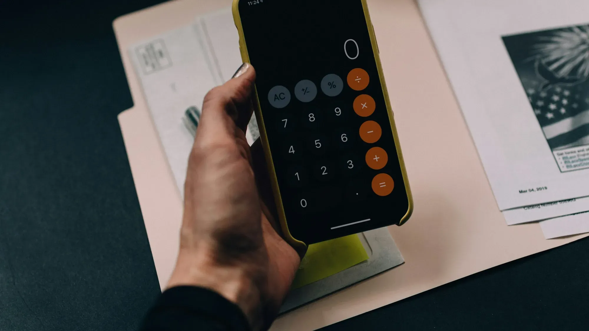 Mano sosteniendo un celular con la calculadora abierta sobre una carpeta