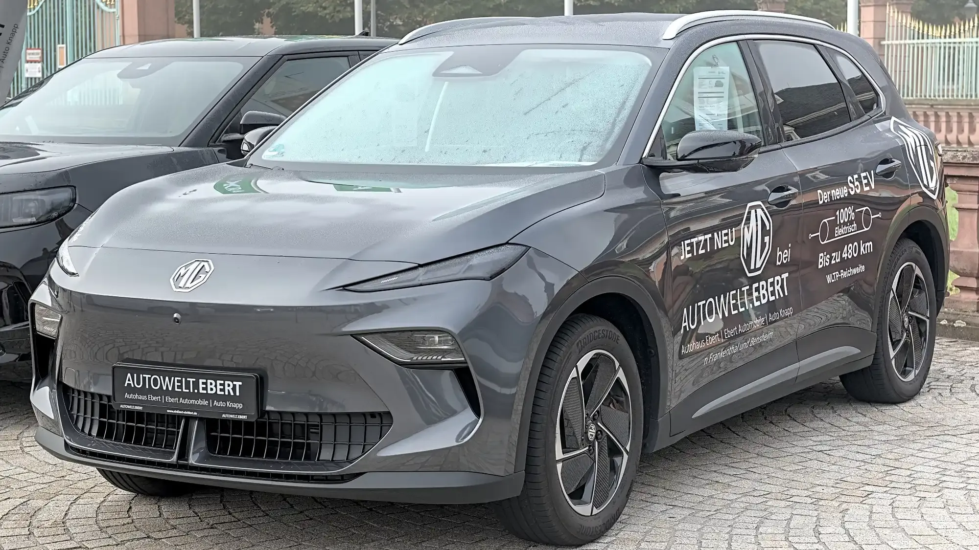 MG S5 EV gris visto de frente y de lado en un evento al aire libre