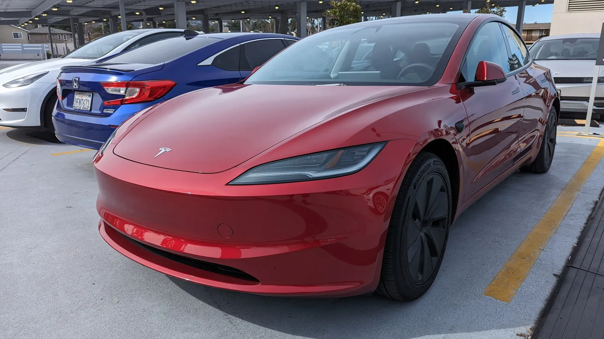 Tesla Model 3 rojo de la generación renovada, visto de frente y de lado