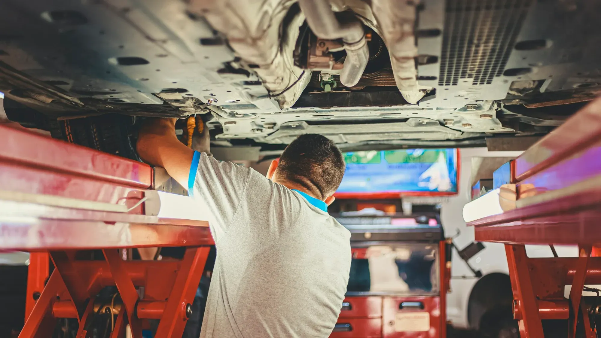 Técnico trabajando debajo de un carro levantado en un elevador de taller